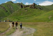 منظر طبيعي في جورجيا يظهر مسافرين في رحلة مشي وسط الجبال الخضراء وآثار تاريخية، وجهة سياحية مميزة للمسافرين من دول الخليج