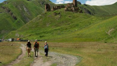منظر طبيعي في جورجيا يظهر مسافرين في رحلة مشي وسط الجبال الخضراء وآثار تاريخية، وجهة سياحية مميزة للمسافرين من دول الخليج